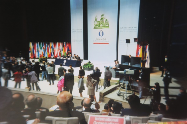 Opening session of a large international conference, with delegates, national flags and speakers gathered on stage.