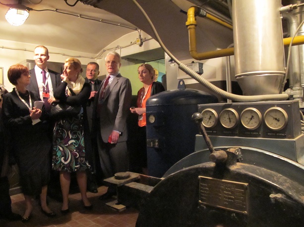 Visitors touring an industrial facility and examining large mechanical equipment and boilers in a plant room.