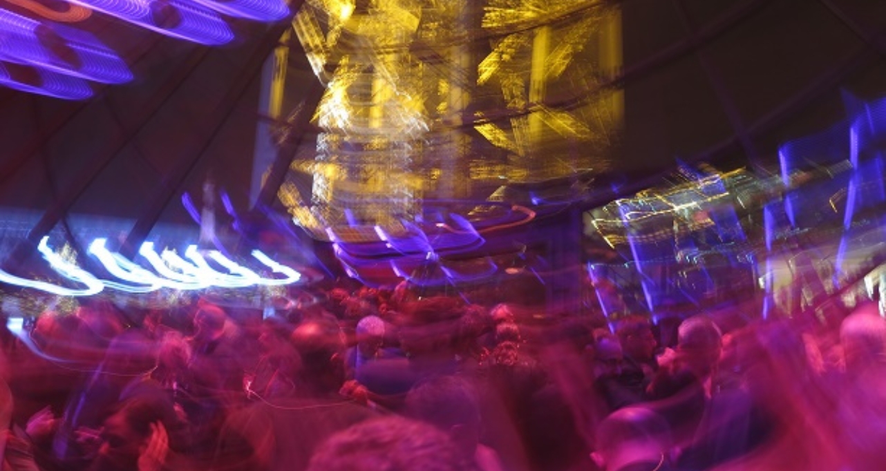 Blurred crowd at a large indoor event under colourful lights.