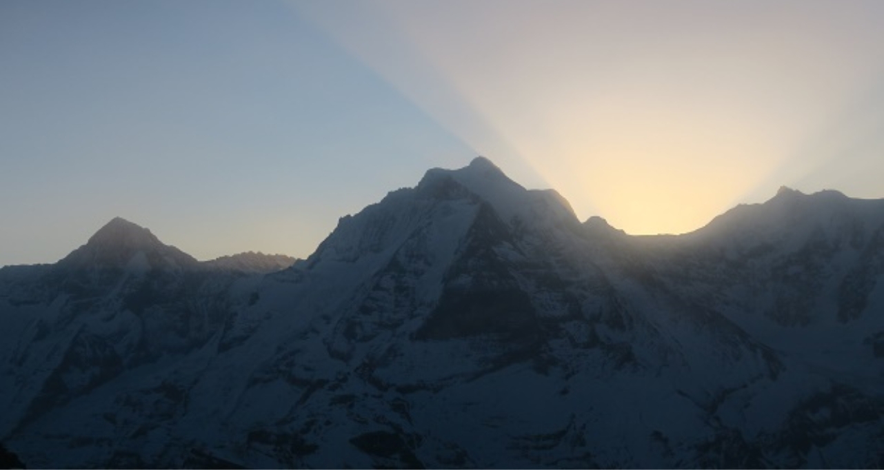 Snow-covered mountain peaks at sunrise, with light breaking over the ridge.