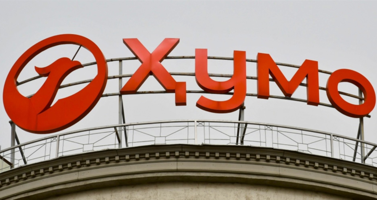 Large red Cyrillic lettering of Humo Bank and a circular bird logo mounted on a curved rooftop beneath a gray sky.