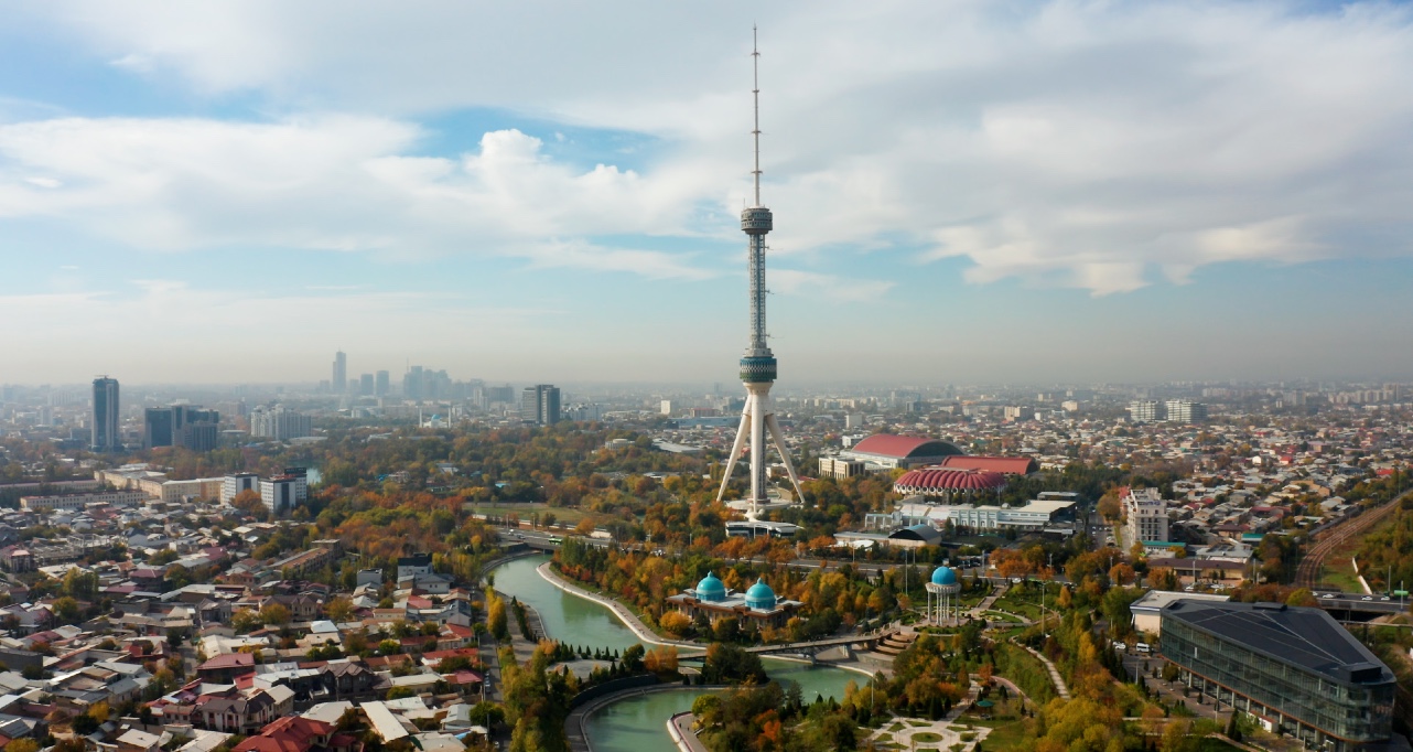 Tashkent TV Tower surrounded by urban landscape, parks, and waterways under a partly cloudy sky