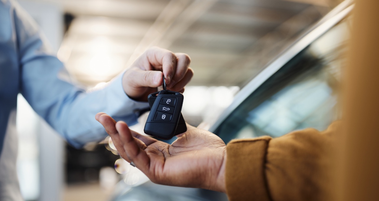 Close up of unrecognizable salesman giving car keys to his black customer in a showroom.