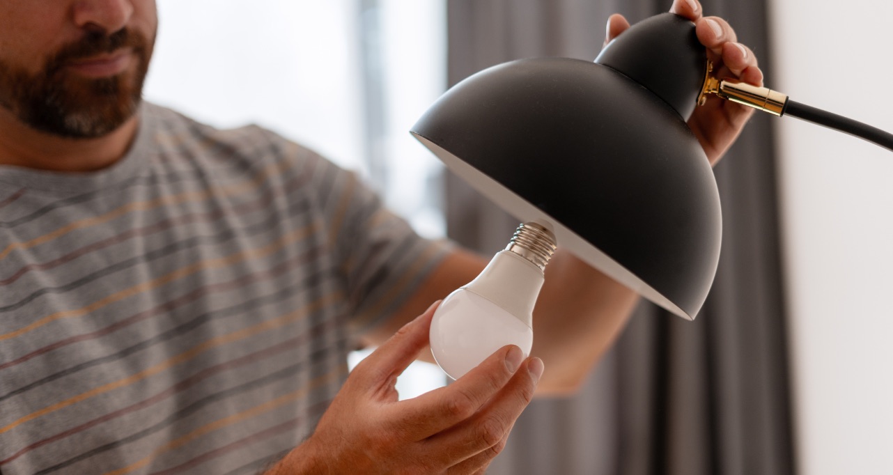 Close-up view of a man carefully installing an energy-efficient LED light bulb into a sleek black modern lamp, enhancing home lighting