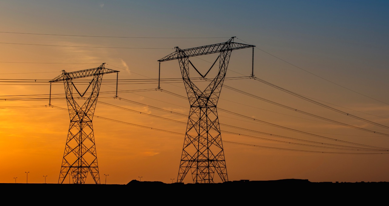 A striking high-contrast image of electricity pylons silhouetted against a fiery orange sunset.