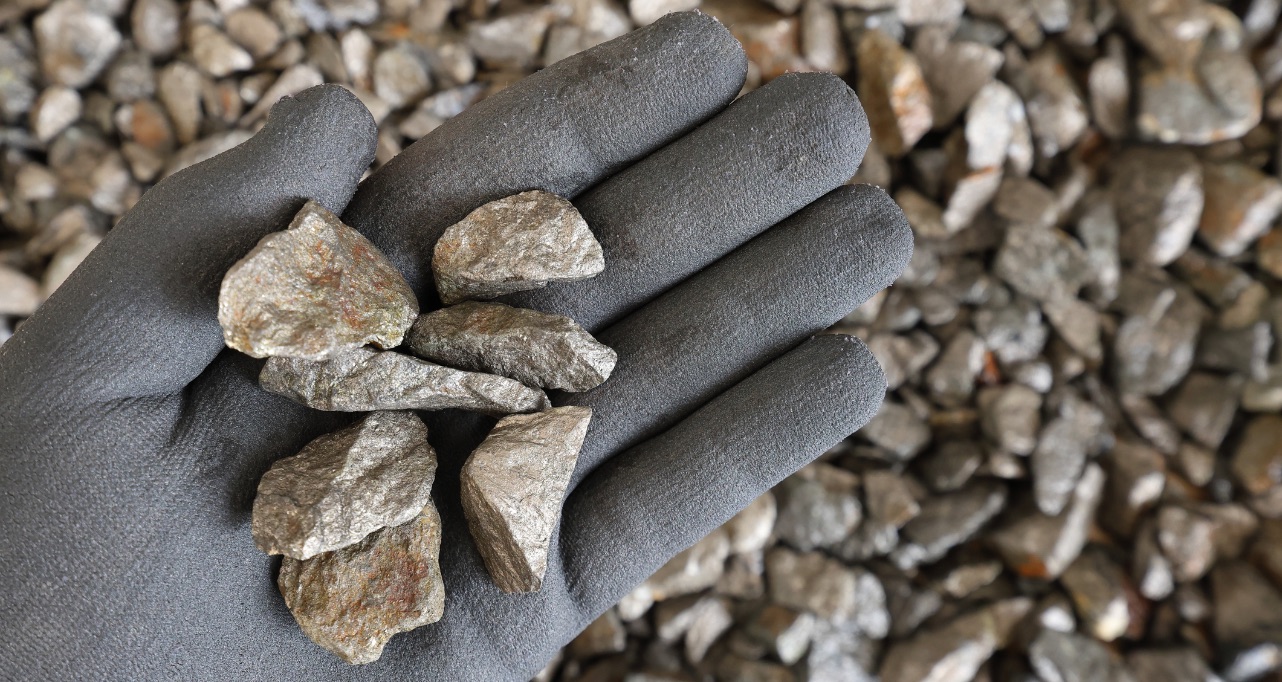 Hand with protective glove holding pieces of pentlandite ore. Rocks, textured. Used in alloys such as stainless steel, nickel-cadmium rechargeable batteries, coins