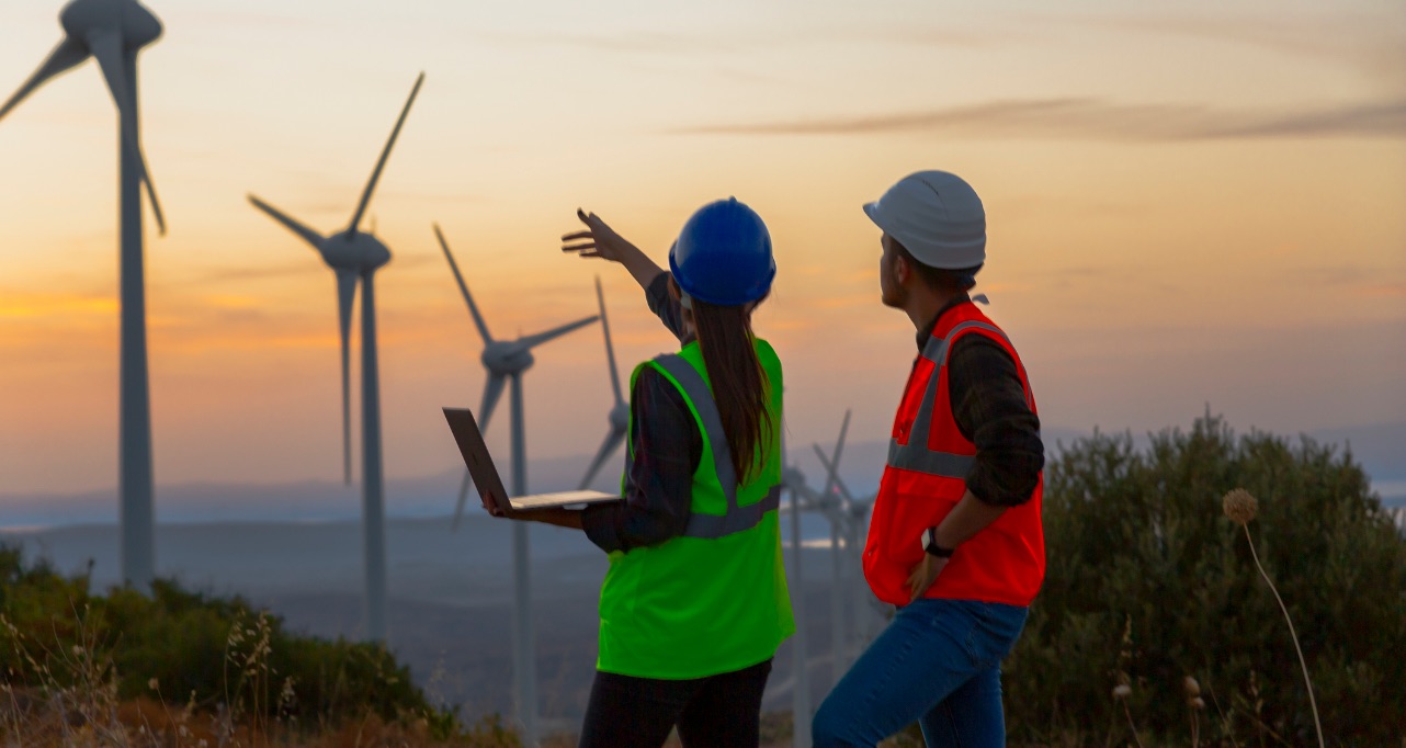 Young maintenance engineer team working in wind turbine farm at sunset
