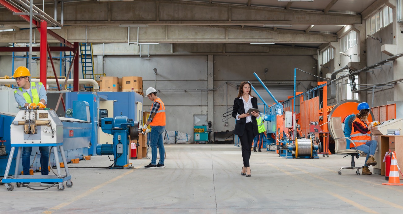 Confident female factory manager wearing business suit walks through a large industrial production hall