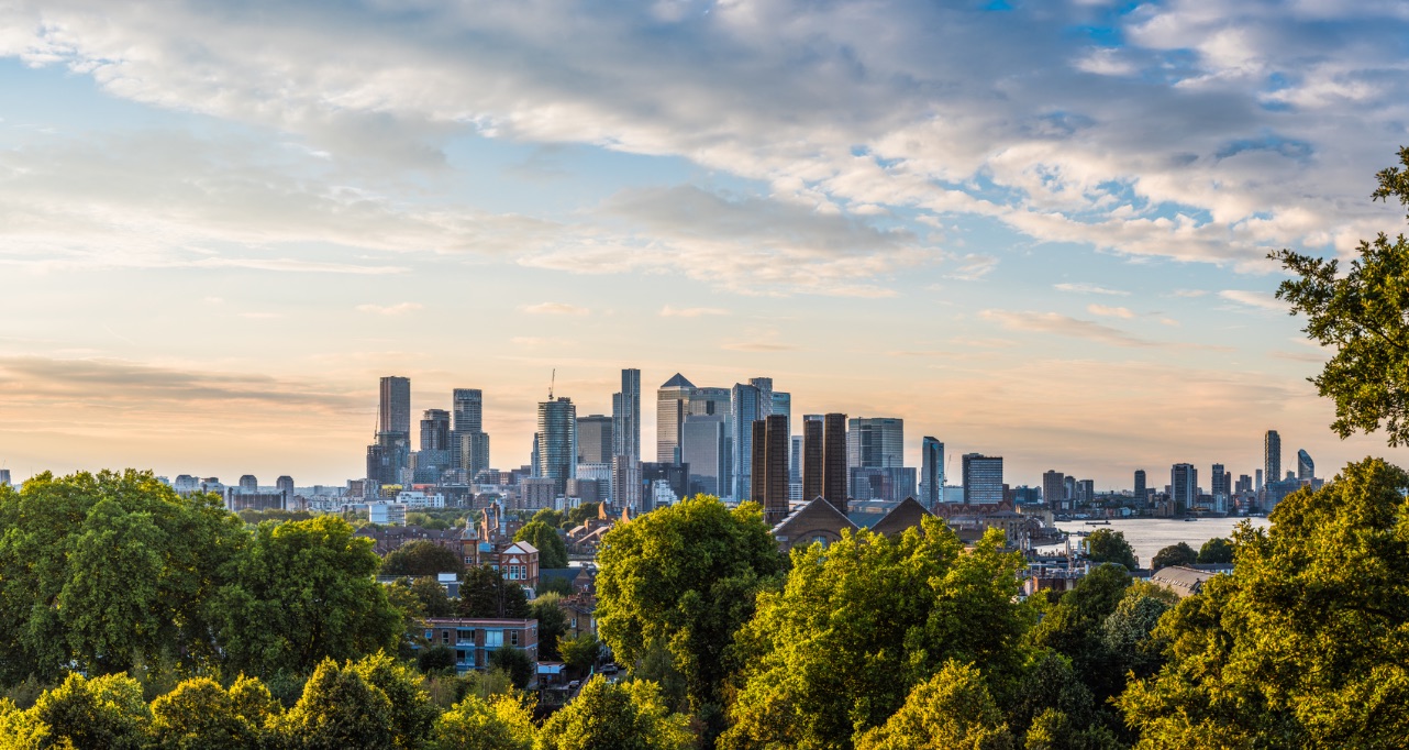 Panoramic view across the trees of Greenwich Park to the high-rise cityscape of Canary Wharf Docklands and the distant skyscrapers of the City of London.